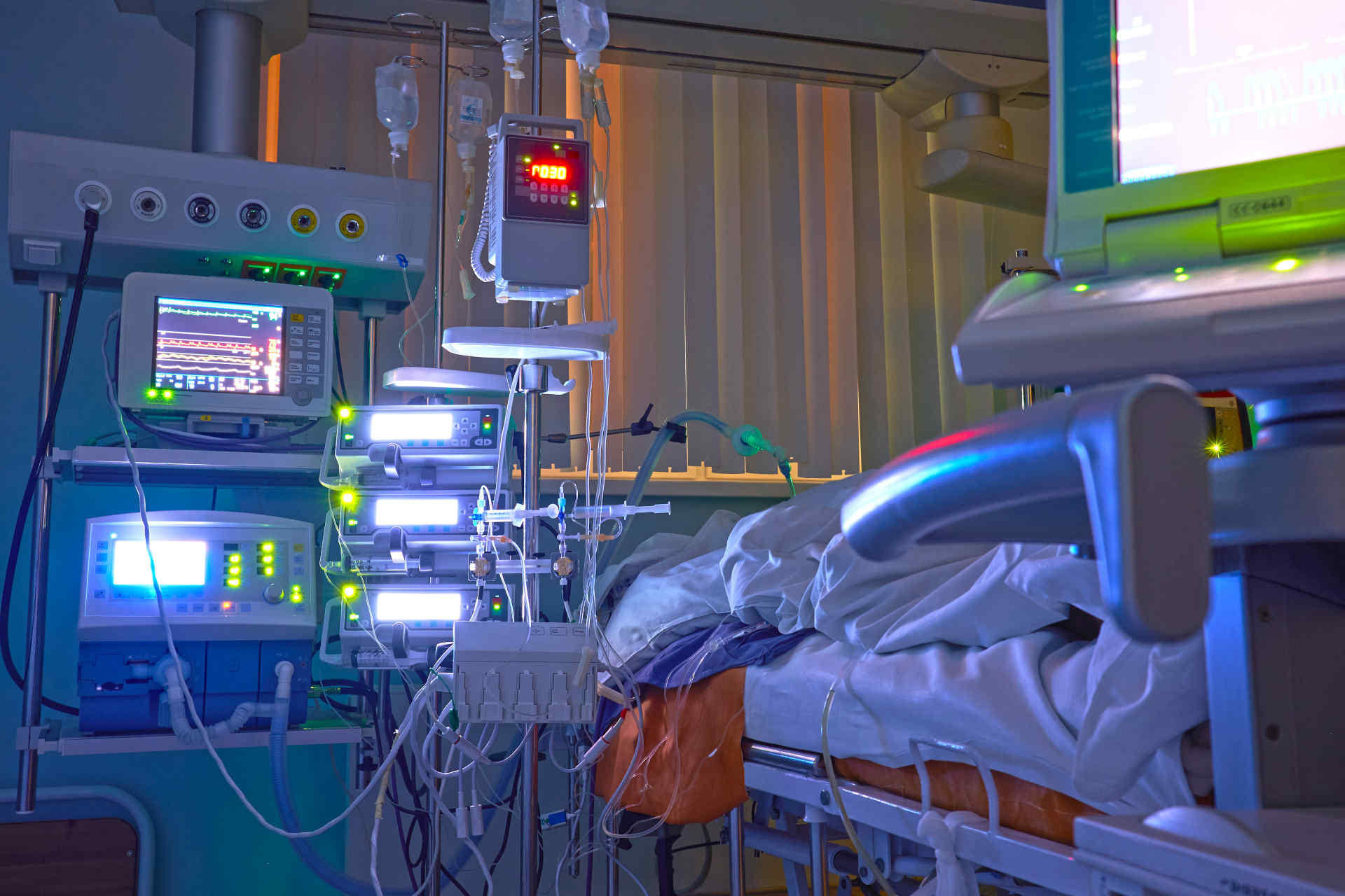 ICU room at night with multiple brightly lit monitors and infusion pumps