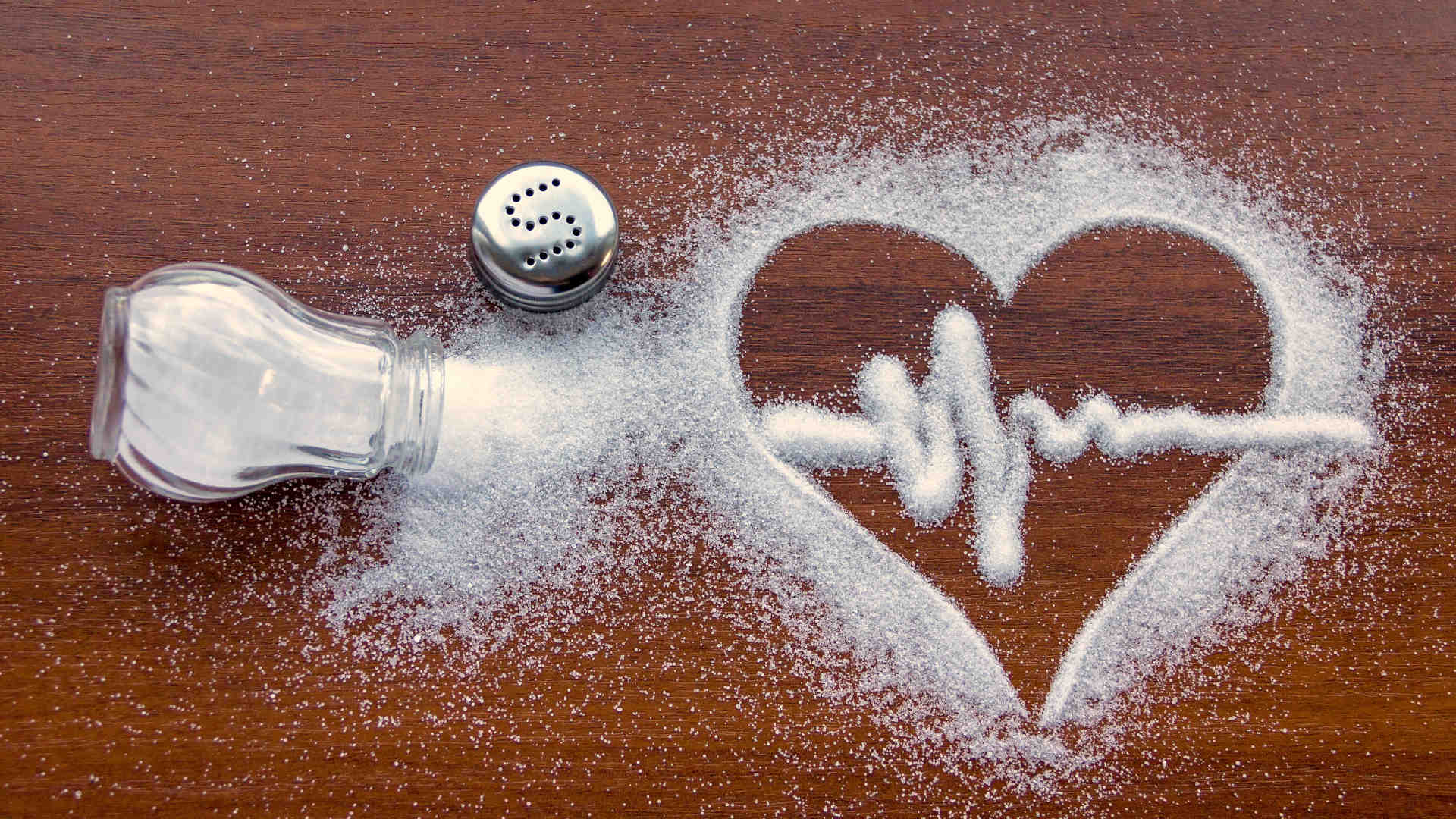 Salt grains on a table, shaped into a heart containing an ECG waveform